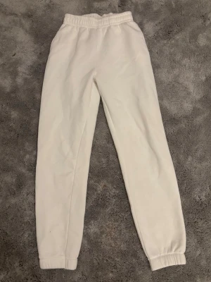 Vita mjukisbyxor med resår - Säljer ett par vita mjukisbyxor med resår i midjan och vid bensluten. Byxorna har en klassisk relaxed fit och är gjorda i mjukt, tjockt material som känns riktigt skönt mot huden. Perfekta för chill dagar hemma eller när du vill ha en clean look. Passar storlek S-M.