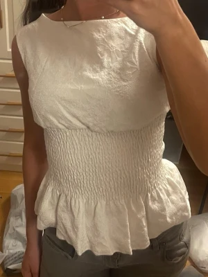 Vit volangtopp - Så fin vit topp med smockad midja och volang nedtill! Helt nytt skick💗