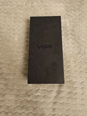 VGR trimmer med mässingsdetaljer - Säljer en elektrisk trimmer från VGR med snyggt graverat mässingsfärgat handtag och detaljerat mönster. Kommer i original svart låda med VGR-logga. Perfekt för hår- och skäggtrimning och har en robust metallkänsla.