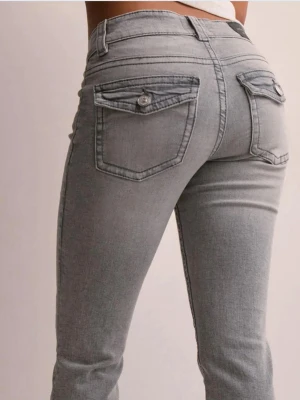 Gina jeans - Snygga grå bootcut jeans med dekorativa fickor bak och knappdetaljer. Jeansen har en klassisk femficksmodell, bälteshällor och är tillverkade i stretchigt denimtyg för skön passform. Perfekta för en trendig och avslappnad look.