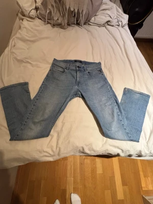 Ljusblå replay jeans - Säljer ett par ljusblå jeans med rak passform och klassisk femficksdesign. Jeansen har bälteshällor, dragkedjegylf och är tillverkade i denim. Perfekta för en avslappnad och stilren look.