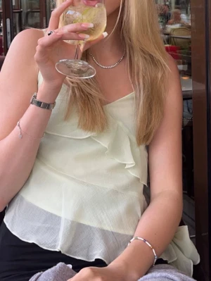 Ljusgrön volangtop från Gina Tricot - Hej!☀️Jag säljer en ljusgrön topp från Gina Tricot med tunna axelband och volangdetaljer framtill och nedtill. Toppen har en asymmetrisk nederkant och en stor rosett på sidan. Endast använd vid två tillfällen💕superfin!!