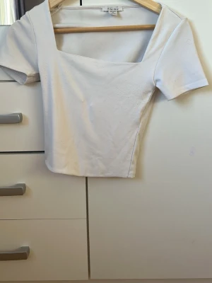 Vit croppad topp från New Yorker  - Snygg vit croppad topp från New Yorker med fyrkantig ringning och korta ärmar. Tillverkad i mjuk bomull med en clean och enkel look som passar till det mesta. Perfekt för dig som gillar minimalistisk stil.