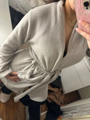 Ljusgrå fluffig morgonrock - Supermjuk och mysig ljusgrå morgonrock i fleece med knytskärp i midjan och långa ärmar. Perfekt för att chilla hemma och hålla sig varm under kalla morgnar. Klassisk modell utan synligt märke.