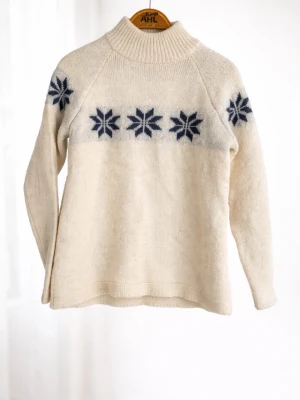 Vit stickad tröja med blått mönster - Vit stickad tröja från MESO med blå snöstjärneliknande mönster över bröstet och ärmarna. Tröjan har hög krage och är tillverkad i ett mjukt, värmande material. Perfekt för kalla dagar och har en klassisk nordisk stil. I ull, liten i storlek 