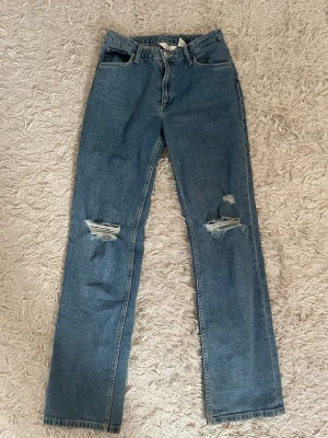 Blå raka jeans med slitna knän - Ett par blå jeans med rak/baggy passform och slitna detaljer vid båda knäna. Jeansen är i storlek 158 och skulle säga att det är en XS/S.