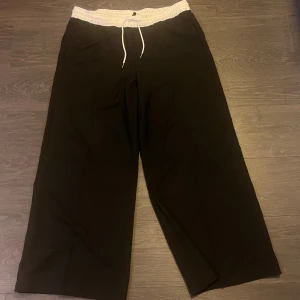Svarta kostymbyxor från H&M - Säljer ett par svarta kostymbyxor med bred, vit resårmidja och vit dragsko från H&M. Byxorna har raka, vida ben och sidofickor. Storlek L, i använt men bra skick.