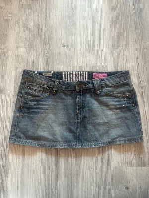 Jeanskjol med stenar  - Snygg kort jeanskjol från Miss Sixty i klassisk blå denim. Kjolen har dekorativa stenar och fickor både fram och bak samt bälteshällor. Perfekt för dig som gillar en cool och avslappnad stil. 