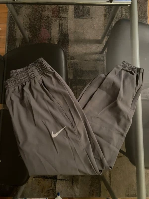 Gråa från Nike - Säljer ett par byxor från Nike med klassisk vit logga på benet. Byxorna har resår i midjan och raka ben, perfekta för chill dagar. Tillverkade i mjukt och bekvämt material som passar till alla avslappnade tillfällen.