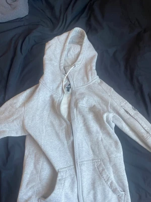 Grå hoodie från Pelle P  - Snygg ljusgrå hoodie från Pelle P med dragkedja framtill, broderad logga på bröstet och fickor på sidorna. Mjuk fleece på insidan och justerbar huva med snören. Perfekt för chill dagar eller när du vill ha en clean look. Kontakta gärna❤️