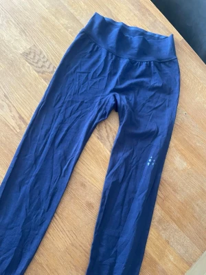 Mörkblå leggings från Craft - Mörkblå leggings från Craft med hög midja och stretchigt material. Diskret logga på benet och smidig passform som sitter skönt. Perfekta för träning eller chill. Snygg och enkel design som funkar till det mesta.