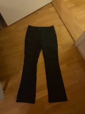 Svarta kostymbyxor från Monki - Känns som S. Snygga svarta kostymbyxor från Monki med klassisk rak passform och lätt utsvängda ben. Byxorna har två knappar i midjan och är tillverkade i ett mjukt tyg som känns bekvämt hela dagen. Perfekta att styla med en skjorta eller crop top.