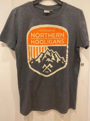 Grå Northern Hooligans t-shirt S - Snygg grå t-shirt från Northern Hooligans med stort tryck framtill i orange och vitt. T-shirten har rund halsringning och korta ärmar. Storlek Small