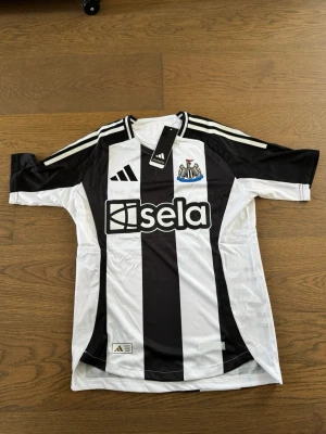 Newcastle United matchtröja Bruno G. - Snygg Newcastle United matchtröja i svart och vitt med klassiska ränder, Adidas-logga och klubbmärke på bröstet. Tryck med 'Bruno G.' och nummer 39 på ryggen. Tillverkad i lätt och ventilerande material, perfekt för fotboll eller träning.