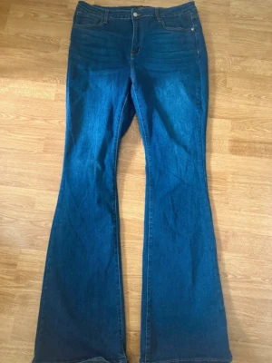 Blå bootcut jeans med hög midja - Snygga blå bootcut jeans med hög midja och klassisk femficksdesign. Jeansen har utsvängda ben och stängs med knapp och dragkedja. Perfekta för en trendig och avslappnad look. Tall Affair Of The Flare Stretch Jeans Dark Wash