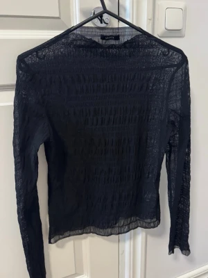 Svart mesh långärmad topp  - Säljer en svart mesh topp  med lång ärm och transparent material. Toppen har en tight passform och är perfekt för att styla lager på lager. Enkel och stilren design som passar till många olika looks.