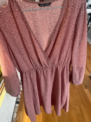 Rosa prickig omlottklänning Shein - Söt rosa kortklänning från Shein med vita prickar och omlott-design. Klänningen har v-ringning, resår i midjan och trekvartsärmar. Perfekt för vår och sommar, lätt och luftig i syntetmaterial.