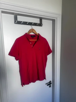 Röd/rosa pikétröja från Ralph Lauren - Klassisk röd/rosa pikétröja från Ralph Lauren med broderad logga på bröstet. Mjuk bomulls material som gör den stretchig.