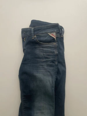 Mörkblå Replay jeans med slitningar - Snygga mörkblå jeans från Replay med coola slitningar och klassisk femficksdesign. Jeansen har kontrastsömmar och Replay-logga på myntfickan. Perfekta för en avslappnad och trendig look.