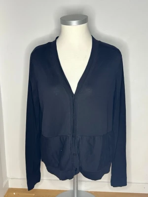 Svart basic kofta med knappar - En svart, tunn och enkel kofta med v-ringning och knäppning framtill. Långärmad och i mjukt material, perfekt att slänga över en t-shirt eller linne. Stilren och passar till det mesta.