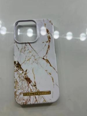 Marmorerat mobilskal Ideal of Sweden - Snyggt mobilskal från Ideal of Sweden med vit marmordesign och guldiga detaljer. Skalet är gjort i hårdplast och har en elegant finish med en guldfärgad logotyp längst ner. Passar perfekt för dig som vill ha en stilren look på mobilen. Kan va lite smuts i några hörn men går lätt att ta bort, Priset kan sänkas vid snabb affär.