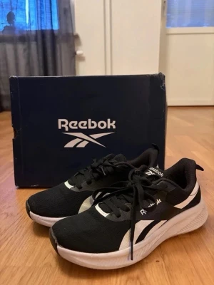 Svarta Reebok sneakers med vit sula - Snygga svarta sneakers från Reebok med vit sula och vita detaljer på sidan. Skorna har klassisk Reebok-logga, svarta skosnören och ovandel i meshmaterial som andas. Perfekta för en sportig och stilren look.