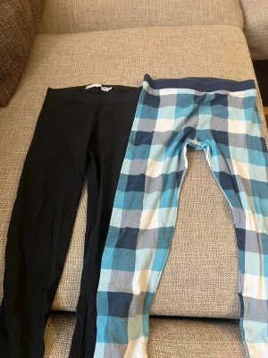 Två par leggings, svart & rutiga - Säljer två par leggings till barn , ett par helsvarta och ett par med blå, vita och svarta rutor. Båda har hög midja och är i stretchigt material, perfekta för en avslappnad och bekväm stil. 