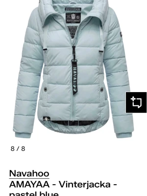 Pastellblå pufferjacka från Navahoo - Snygg pastellblå pufferjacka från Navahoo med huva och dragkedja framtill. Jackan har ribbade muddar, två sidofickor med knappar och coola detaljer på dragkedjan. Insidan har flera praktiska fickor och ett unikt tryck. Perfekt för kalla vinterdagar.