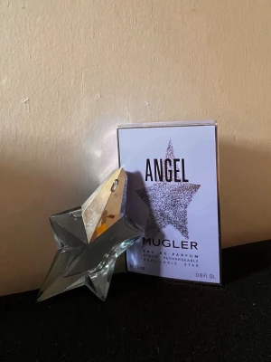 Angel Eau de Parfum från Mugler - Angel Eau de Parfum från Mugler i en ikonisk stjärnformad flaska av glas med silverfärgade detaljer. Doften är intensiv och unik, och flaskan är både snygg och samlarvänlig. Förpackningen är ljuslila med en glittrig stjärna på framsidan.