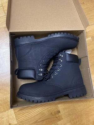 Svarta kängor från Everest - Tuffa svarta kängor från Everest med grov sula och metallhål för snörning. Kängorna är tillverkade i ett slitstarkt syntetmaterial och har en klassisk, robust design som passar perfekt till höstens och vinterns outfits.