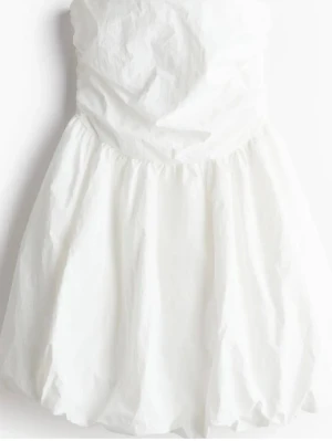 Vit axelbandslös kortklänning - Slutsåld hm puff klänning. Snygg vit axelbandslös kortklänning med ballongformad kjol och rynkad överdel. Perfekt för dig som vill ha en stilren och fräsch look. Klänningen har en enkel men trendig design som passar till många tillfällen.