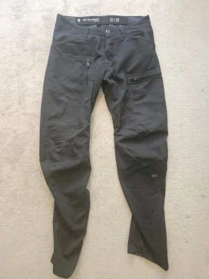 Svarta cargobyxor från G-Star RAW - Svarta cargobyxor från G-Star RAW med flera praktiska fickor, bland annat en med dragkedja på låret. Byxorna har en modern, rak passform och är tillverkade i ett slitstarkt material. Perfekta för en avslappnad och cool stil.