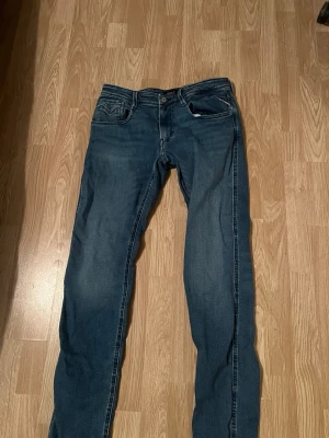 Blå jeans från Replay  - Säljer ett par klassiska blå jeans från Replay med raka ben och fem fickor. Jeansen har snygga detaljer på bakfickorna och en mörk tvätt som passar till det mesta. Materialet är mjukt denim som ger en skön känsla och bra passform. Det är storlek 32W och 34 längd