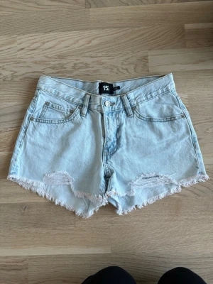 Ljusblå denimshorts från 157 - Säljer två par blåa denimshorts från 157 med fransig kant och klassisk femficksmodell. Shortsen har låg midja. Helt oanvända, ljusblåa paret använd vid ett tillfälle