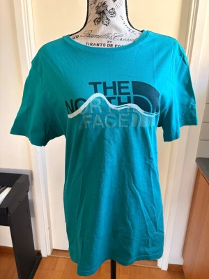 Turkos T-shirt från The North Face - Snygg turkos T-shirt från The North Face med tryckt logga framtill i blått och vitt. Klassisk rund halsringning och korta ärmar. Perfekt för en avslappnad och sportig stil.
