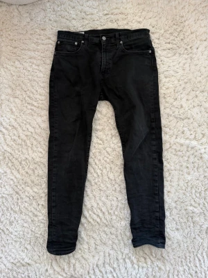 Svarta slim jeans från Levi's - Säljer ett par svarta slim jeans från Levi's med klassisk femficksdesign och knappgylf. Jeansen har en slim passform och är tillverkade i stretchigt denimtyg för extra komfort. Perfekta till en avslappnad streetwear-look.