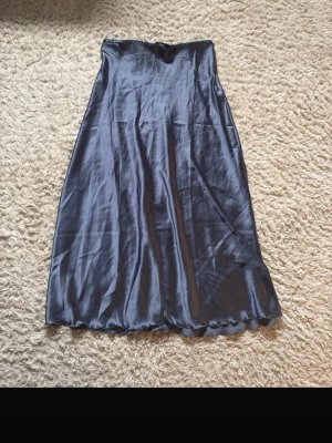 Mörkblå satinkjol från The Black Label - Snygg långkjol i mörkblå satin från The Black Label Collection. Kjolen har en glansig finish och ett enkelt. Aldrig använd