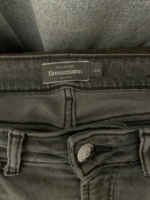 Grå jeans från Dressmann - Snygga grå jeans från Dressmann med klassisk femficksmodell och raka ben. Jeansen har en diskret tvättad look och är tillverkade i ett mjukt denimtyg som ger en avslappnad känsla. Perfekta för dig som gillar stilrena och enkla jeans.