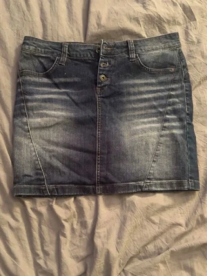 Blå jeanskjol med fickor - Snygg blå jeanskjol i klassisk modell med fram- och bakfickor samt bälteshällor. Kjolen har knappar och dragkedja framtill och är lätt tvättad för en cool look. Perfekt att matcha med en t-shirt eller hoodie.