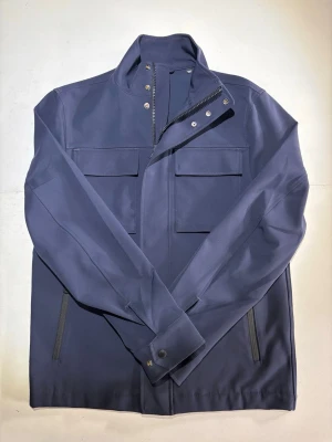 Mörkblå vindjacka med fickor - Marinblå field jacket från J.Lindberg med hög krage, dragkedja och tryckknappar framtill. Två bröstfickor med lock och två sidofickor med dragkedja. Storlek: XS men passar mer som en S. Skick 9,5/10. 