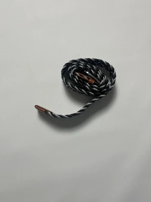 Flätat bälte med mönster storlek 100cm - Snyggt flätat bälte i svart, vitt, mörkblått och grått med bruna läderdetaljer vid spännet och änden. Perfekt accessoar för att lyfta din outfit med en cool och modern touch. Bältet har ett klassiskt spänne i metall och passar till både jeans och chinos. Storlek 100cm