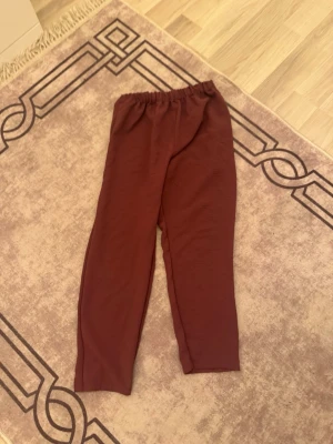 Vinröda mjukisbyxor från Telvin - Mysiga vinröda mjukisbyxor från Telvin Collection med resår i midjan. Byxorna har en enkel och avslappnad passform, perfekta för chill dagar hemma. Tillverkade i ett mjukt och stretchigt material som känns skönt mot huden.