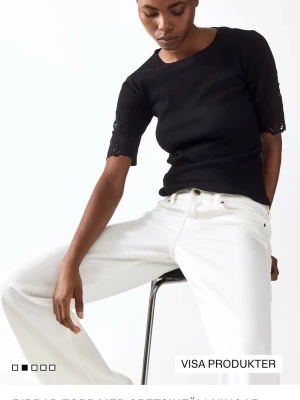 Svart topp med spetsärmar - Stilren svart topp med rund hals och korta ärmar i spets. Toppens passform är normal och materialet ser ut att vara mjukt och stretchigt, perfekt för en clean och modern look.