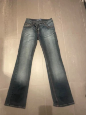 Blå bootcut jeans med slitningar - Snygga låga blå bootcut jeans med lätt slitna detaljer och snygga fickor. Perfekta för dig som gillar en avslappnad och trendig stil. Hon på bilden är 162 cm. Midjemått rakt över ca 35 cm. Innerbenslängd ca 80 cm