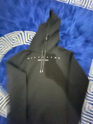 Emporio armani hoodie Herr - Säljer en svart hoodie från Emporio Armani med vitt tryck över bröstet. Hoodien har en stor huva med dragsko och klassisk passform. Perfekt för dig som gillar streetwear och vill ha en enkel men snygg look.