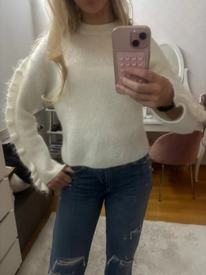 Vit stickad tröja Arket - Säljer en vit stickad tröja med rund hals och långa ärmar. Tröjan har coola fransdetaljer längs ärmarna som ger en trendig look. Perfekt att matcha med jeans för en avslappnad stil.