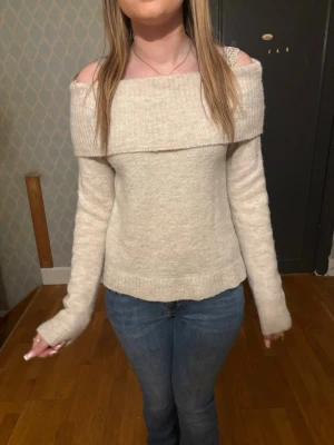 Off shoulder stickad tröja beige - Snygg off shoulder stickad tröja i beige med bred krage som vilar över axlarna. Tröjan har långa ärmar och är gjord i ett mjukt, mysigt material. Perfekt för dig som vill ha en trendig och bekväm look.