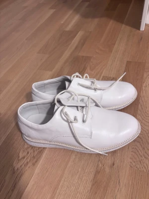 Gram skor  - Snygga vita loafers i läder med klassisk snörning och rund tå. Skorna har en stilren design med ljusa sömmar och låg sula. Perfekta för dig som gillar en clean och modern look. Har också svarta snören ifall man vill byta. Helt oanvända