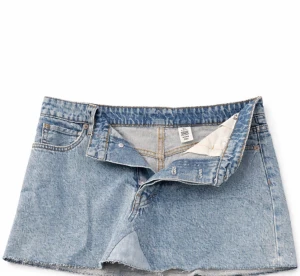 Blå jeanskjol med fjärilsdetaljer - Trendig blå jeanskjol från H&M med två bakfickor. Kjolen har snygga fjärilsdetaljer på ena bakfickan och klassisk knapp- och dragkedjestängning framtill. Fjärils detaljerna är lite slitna och de är omgjord från shorts till kjol och därför inte helt rak nedtill. I stolek 36. 