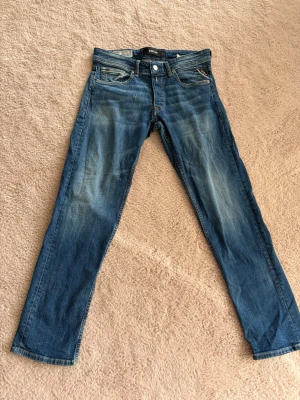 Blå Replay jeans med slitningar - Snygga blå jeans från Replay med klassisk femficksmodell och diskreta slitningar framtill. Jeansen har raka ben och normal midja. Materialet är denim i bomull med en skön känsla. Perfekta för en avslappnad och trendig look. Litet hål lite över högra låret men det är lätt att sy igen.